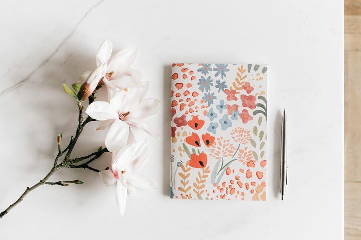 A patterned notebook and pen beside pale flowers